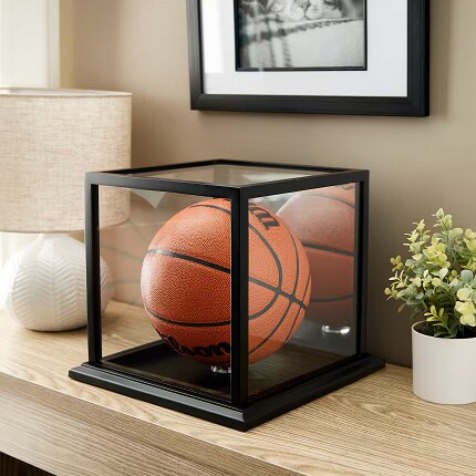 basketball in black framed case on wood table next to lamp