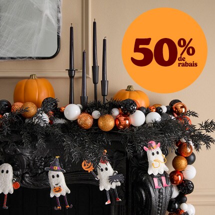 Salle violette foncée avec une cheminée décorée pour Halloween et des bougies noires suspendues.