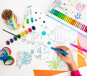 Child drawing an underwater scene with paint and markers spread across the drawing