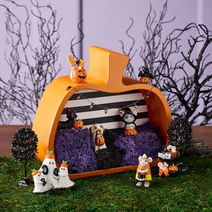 Pumpkin-shaped diorama featuring small animal figurines dressed in costumes, surrounded by miniature trees and purple moss inside the pumpkin. 