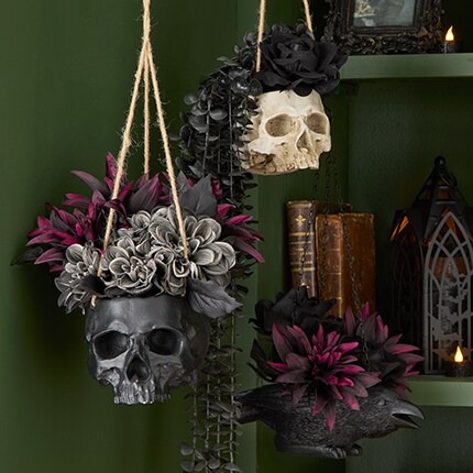 Black pot with dark colored roses and a pot in the shape of skeleton hands grabbing a red heart.