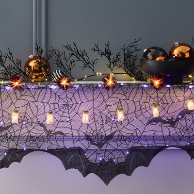 Halloween themed fireplace with mini ghost in jars and orange burst string lights, black cobweb with lit mantle scarf and Halloween themed ornaments