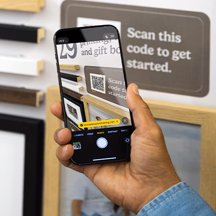 A hand holding up a phone and taking a photo of frames on a wall.