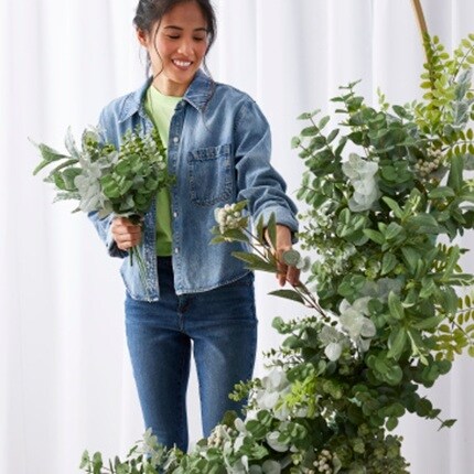 woman attaching greenery to arch arrangement