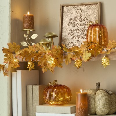 Fall themed bookshelf with lit glass orange pumpkins fall candles and fall leaf garland