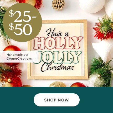 MakerPlace by Michaels Festive image with "Have a Holly Jolly Christmas" sign, surrounded by pine cones, red and white ornaments. Price shown as $25-$50. "Shop Now" button below.