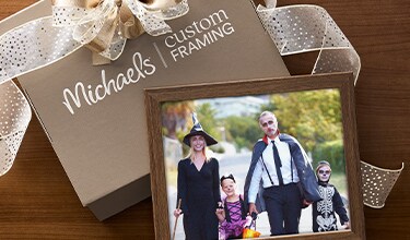 A wrapped gift with Michaels Custom Framing branding with a family photo leaning on it.