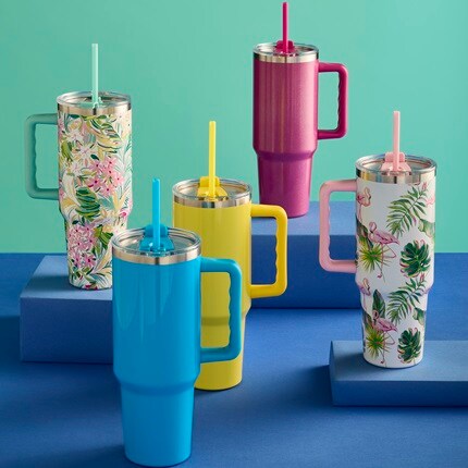 A floral tumbler, solid pink, solid yellow, solid light blue, and a tropical flamingo tumbler sitting on a blue table. 