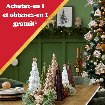 Salle verte avec des rennes et des chaussettes accrochés au mur, un sapin de Noël décoré et une table en bois ornée de petits arbres en céramique.