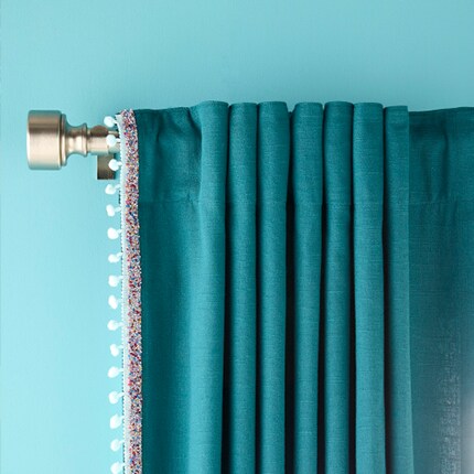 teal curtain with white trim on brushed gold rod on blue wall