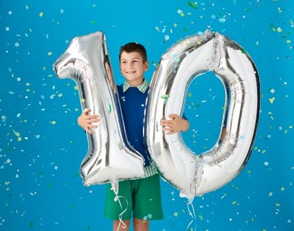 young boy holding number one and number zero balloons with blue confetti background