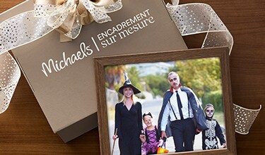 A wrapped gift with Michaels Custom Framing branding with a family photo leaning on it.