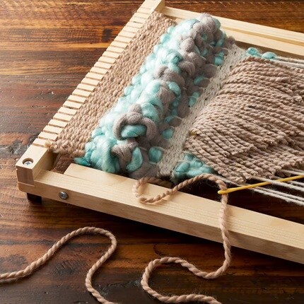 Métier à tisser sur une table en bois avec un projet de fil marron et bleu clair.