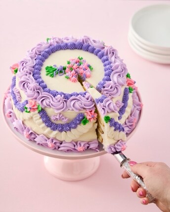 hand cutting ornately decorated cake with purple icing