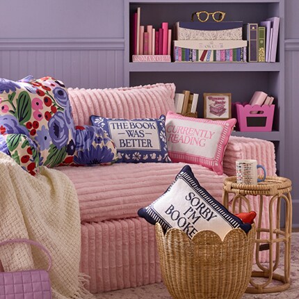 Canapé rose avec des coussins à thème de lecture et étagère violette avec des accents de livres.