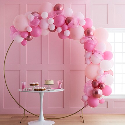 pink room with gold arch filled with balloons in shades of pink and white treat table
