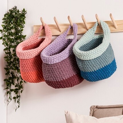 three yarn baskets hanging from wood peg hooks in pink, purple and blue shades