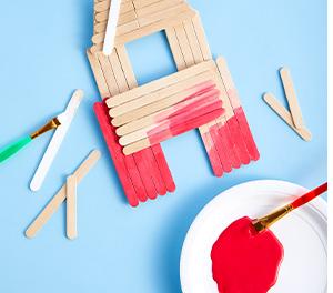 Popsicle sticks being crafted to create a red house on a blue background