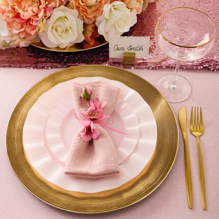 gold charger and silverware with pink plates and pink napkin tied with ribbon