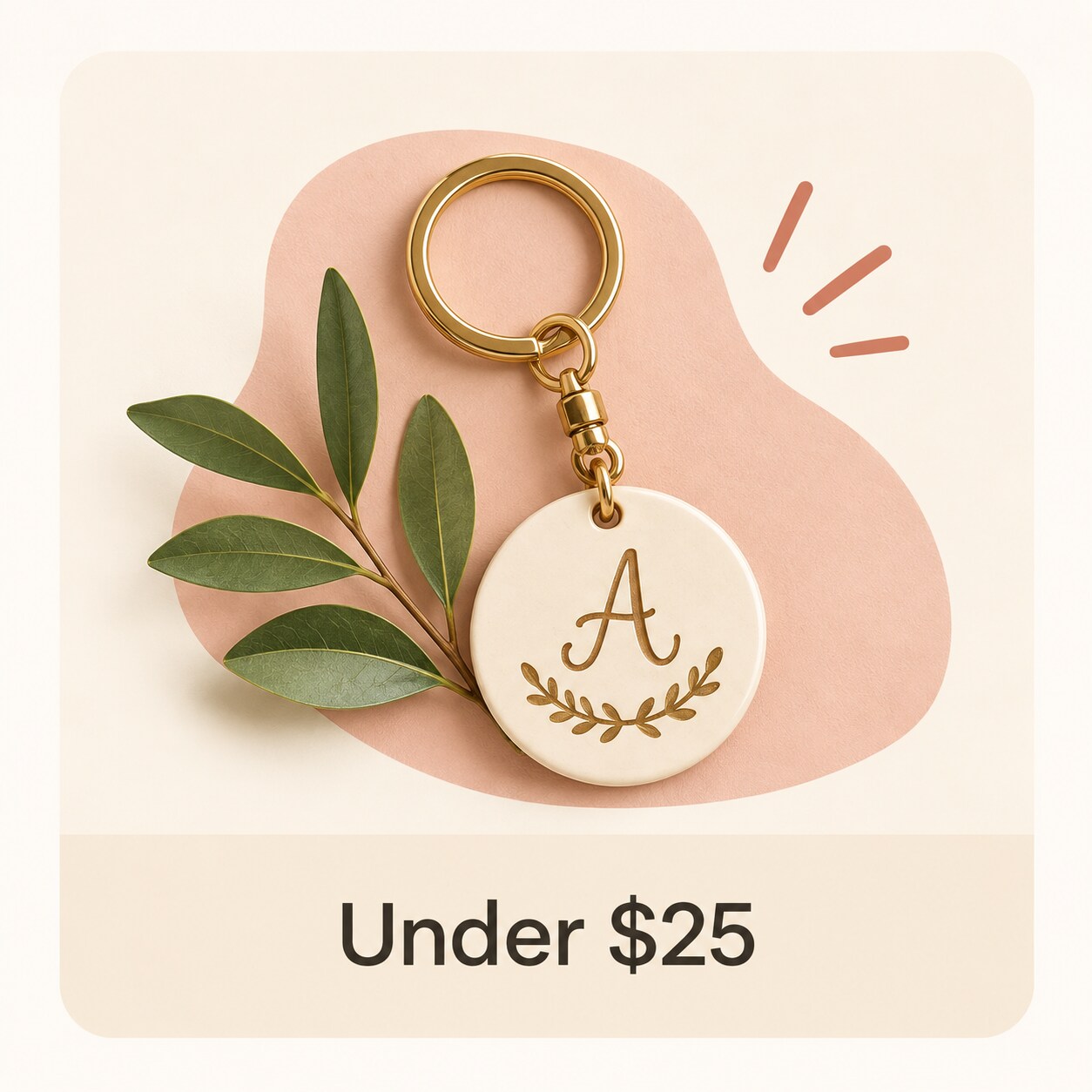 MakerPlace by Michaels Gold keychain with a cream round pendant engraved with “A” and a laurel wreath, on a pink backdrop with sparkles; price range $10–$25.
