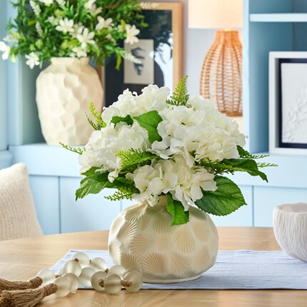 White hydrangeas and green foliage on a wooden table. 