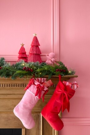 pink and red stockings hanging from wood mantel with green garland