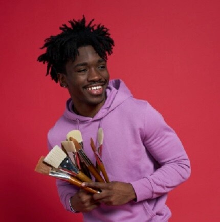 man holding paint brushes in purple sweatshirt with red background