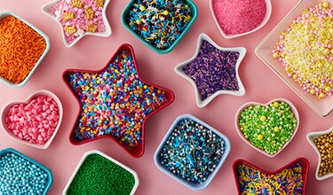 assorted sprinkles in star, heart and square ramekins on pink table