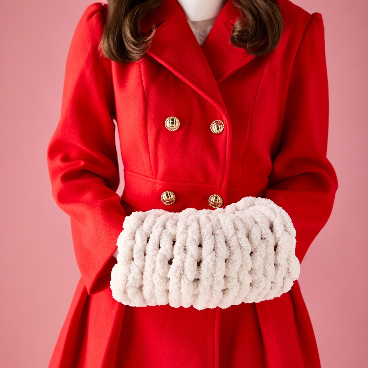 A woman wears a red coat with a fuzzy yarn muff around her hands.