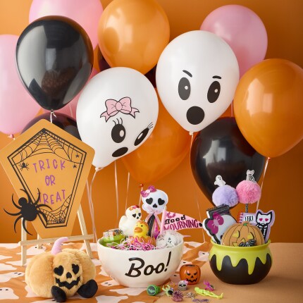 Halloween balloons behind a table. Halloween kids toys sitting on the table in halloween buckets. 