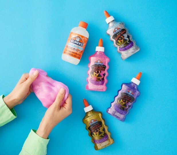 Glue laying on a blue background with hands making slime