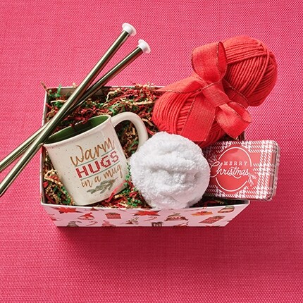 knitting needles, yarn, mug in a holiday gift basket