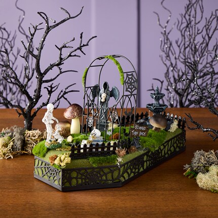 Coffin-shaped base decorated with green moss, mushrooms, a skeleton, and a black fence with spiderweb designs.