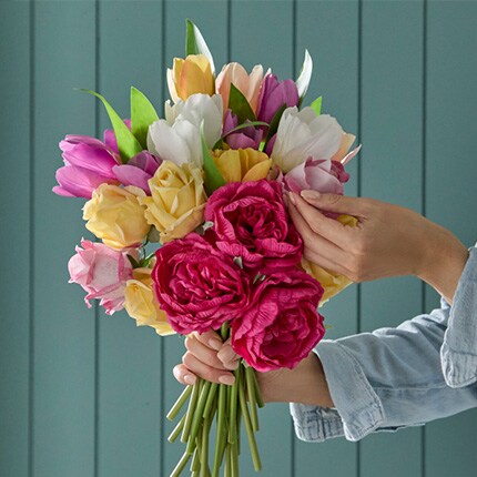 hand touching bouqet of pink, yellow and purple flowers