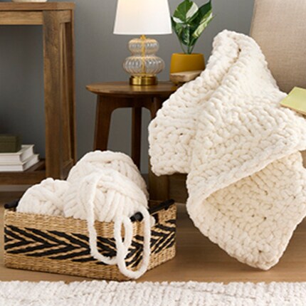 ivory crocheted blanket on chair next to whicker basket with skeins of yarn