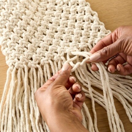 mains tressant un cordon en macramé couleur crème