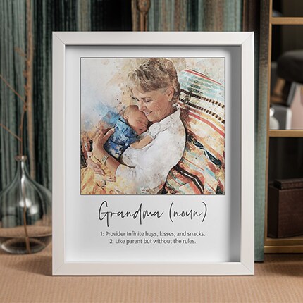 MakerPlace by Michaels Framed watercolor-style print of a grandmother cuddling a sleeping baby, with a playful definition of “Grandma” below; warm, loving tone.
