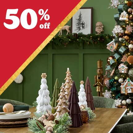 green room with reindeer and stockings on wall, with decorated Christmas tree and wood table with ceramic tree accents with 50% off in white text in red triangle