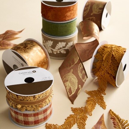 Decorative ribbon spools in gold, brown, green, and cream, with lace and leaf patterns scattered on a warm beige surface, creating a cozy tone.