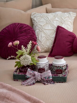 burgandy and white pillows on bed with floral tray and candles