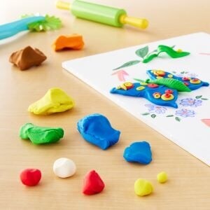 Various colors of shaped clay on a wood table with tools in the background.