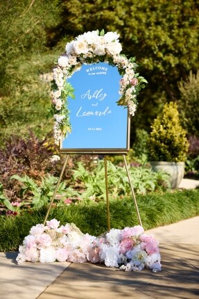 gold easel with mirror welcome sign decorated with flowers