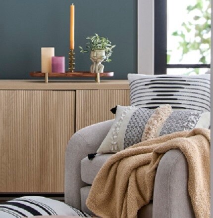 chair with blanket and pillows in front of light wood console with candles