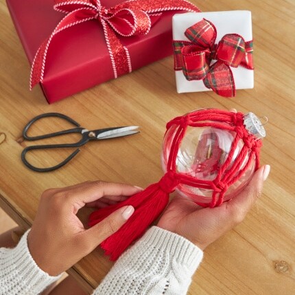 hand holding clear ornament wrapped in red yarn