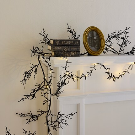 White mantel decorated with black branch-like garlands and small warm white string lights. 