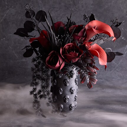 Floral arrangement in a vase adorned with raised skull designs. 