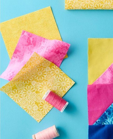 square cuts of fabric on a blue background with 2 thread spools