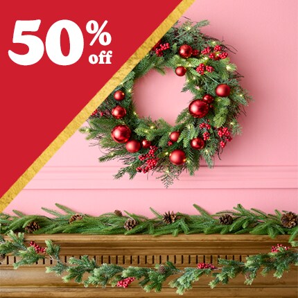 green wreath with red ornaments on pink wall above wood mantel with evergreen garland with 50% off in white text over red triangle