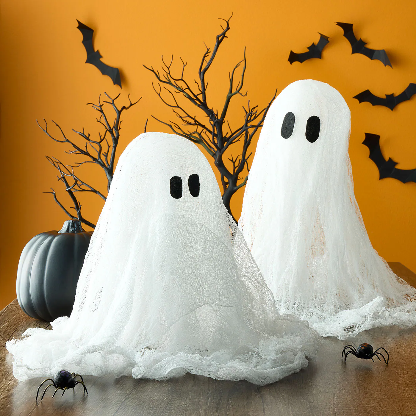 Ghosts made of cheesecloth on an orange background with bats