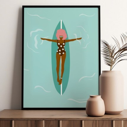 MakerPlace by Michaels Framed minimalist wall art shows a stylized woman floating on a teal surfboard in turquoise water, beside neutral vases and dried palm leaves.